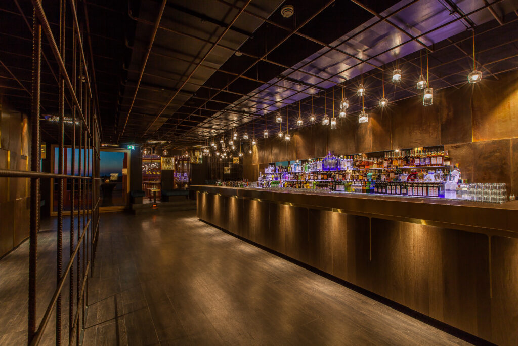 Elegante Bar mit beleuchtetem Regal, dunklem Holz und stimmungsvollem Licht. Modernes Design und stilvolle Atmosph&auml;re.
